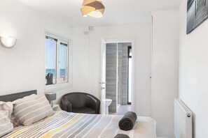 Un dormitorio con cama, una silla, una lámpara, una ventana con vistas al mar y una puerta que da a otra habitación.
