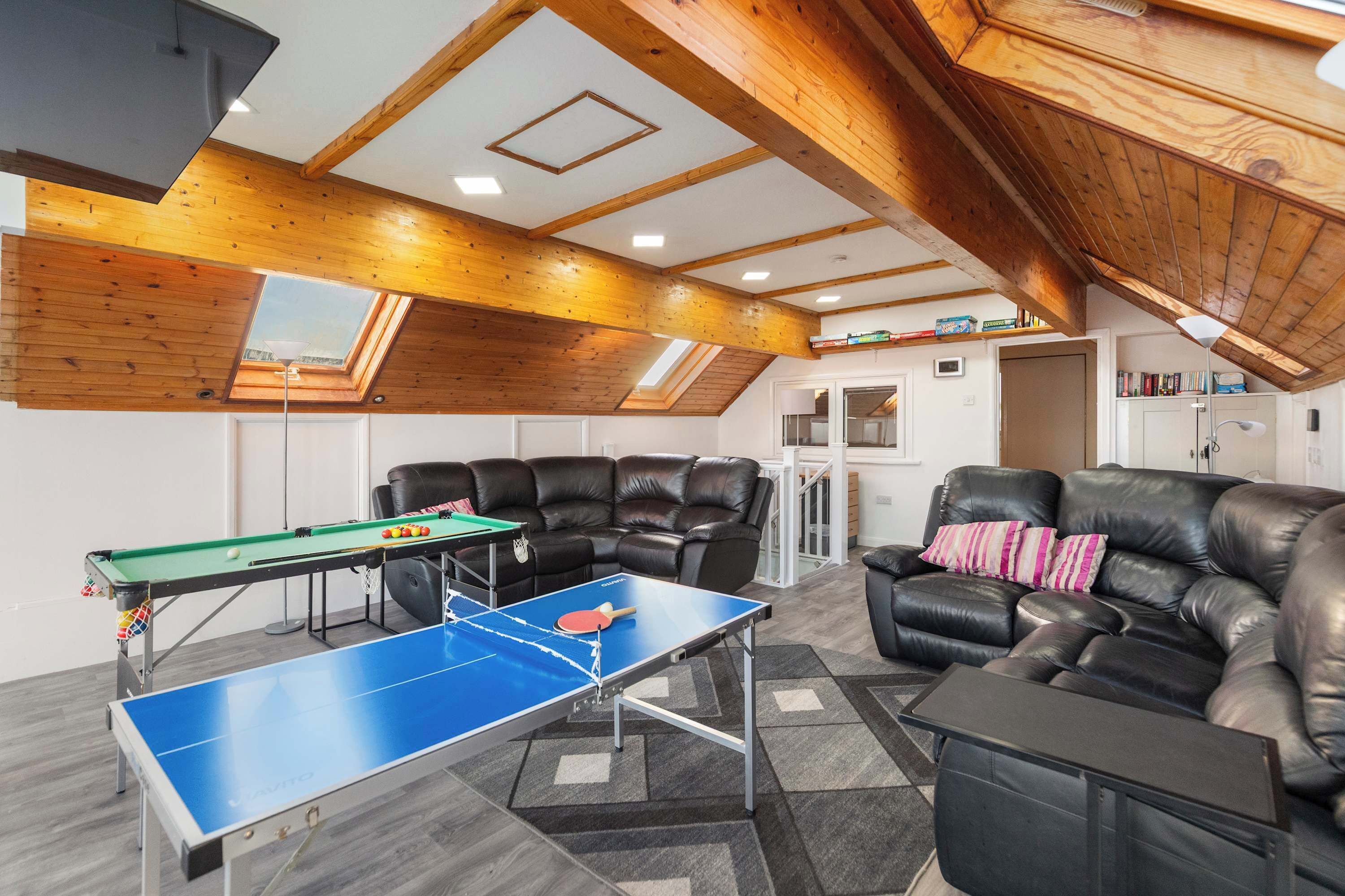 A room with a ping pong table, leather sofas, a bookshelf, and a skylight.