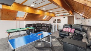 A room with a ping pong table, leather sofas, a bookshelf, and a skylight.
