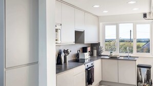 A modern kitchen with white cabinets, a built-in microwave, a stove, and a window with a view of greenery.