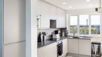 A modern kitchen with white cabinets, a built-in microwave, a stove, and a window with a view of greenery.