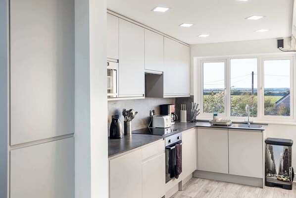 A modern kitchen with white cabinets, a built-in microwave, a stove, and a window with a view of greenery.