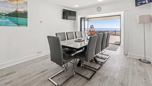 A conference room with a table and chairs, a TV mounted on the wall, and a view of the sea through an open door. - Oceanfront Beach House - Family-Friendly (Pevensey)