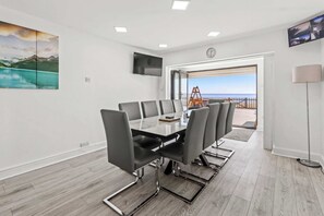 Une salle de conférence équipée d’une table et de chaises, d’un téléviseur fixé au mur, et offrant une vue sur la mer par une porte ouverte.