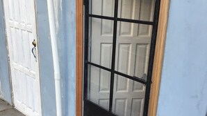 Una puerta con panel de vidrio y marco de madera, un felpudo y una puerta blanca al fondo.