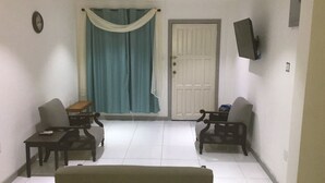 Una habitación con dos sillas de madera, una mesita, un televisor en la pared y una puerta.