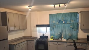 Una cocina compacta con estufa a gas, armarios, un lavamanos y un taburete de bar.