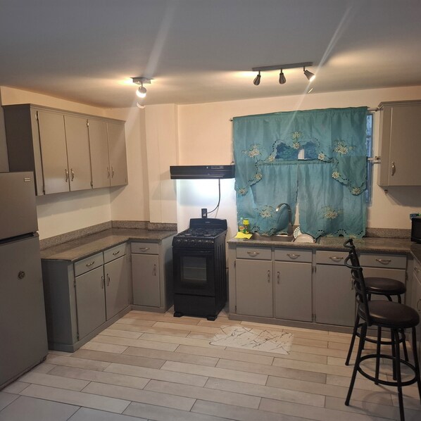 A compact kitchen with a gas stove, cabinets, a sink, and a bar stool. - Gated community apt in residential area  (Georgetown)