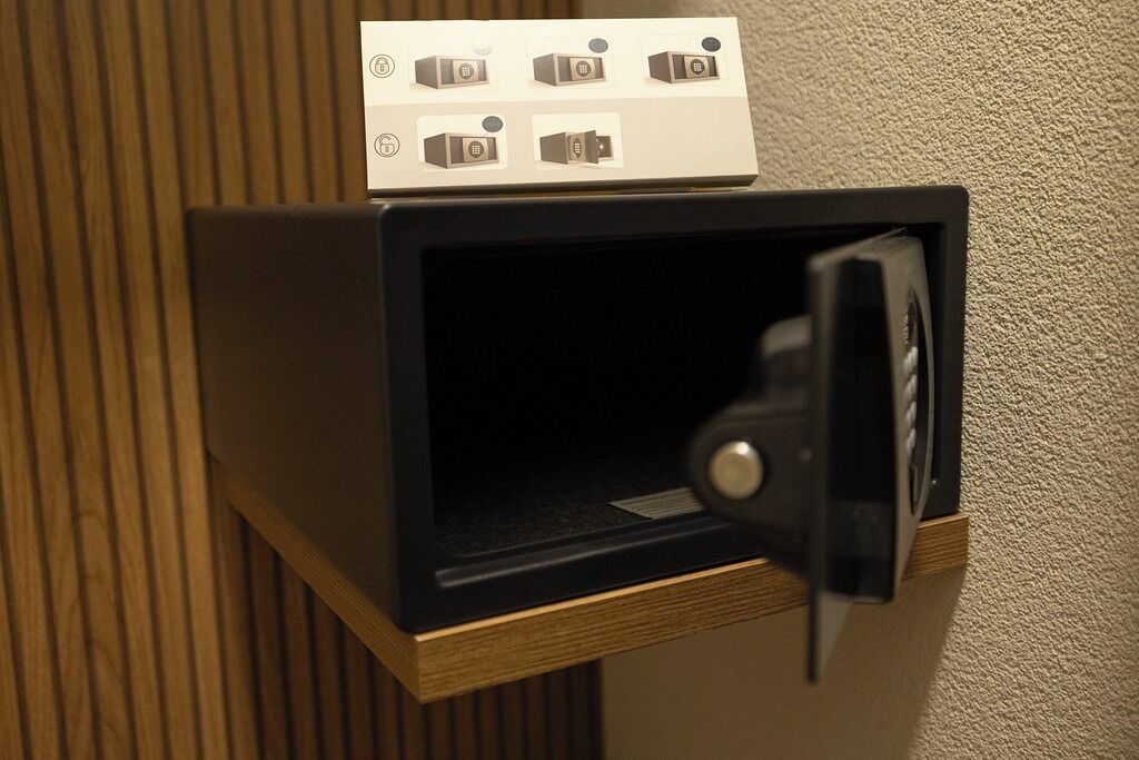 A black minibar with a control panel on top, a wooden base, and a textured wall behind it.