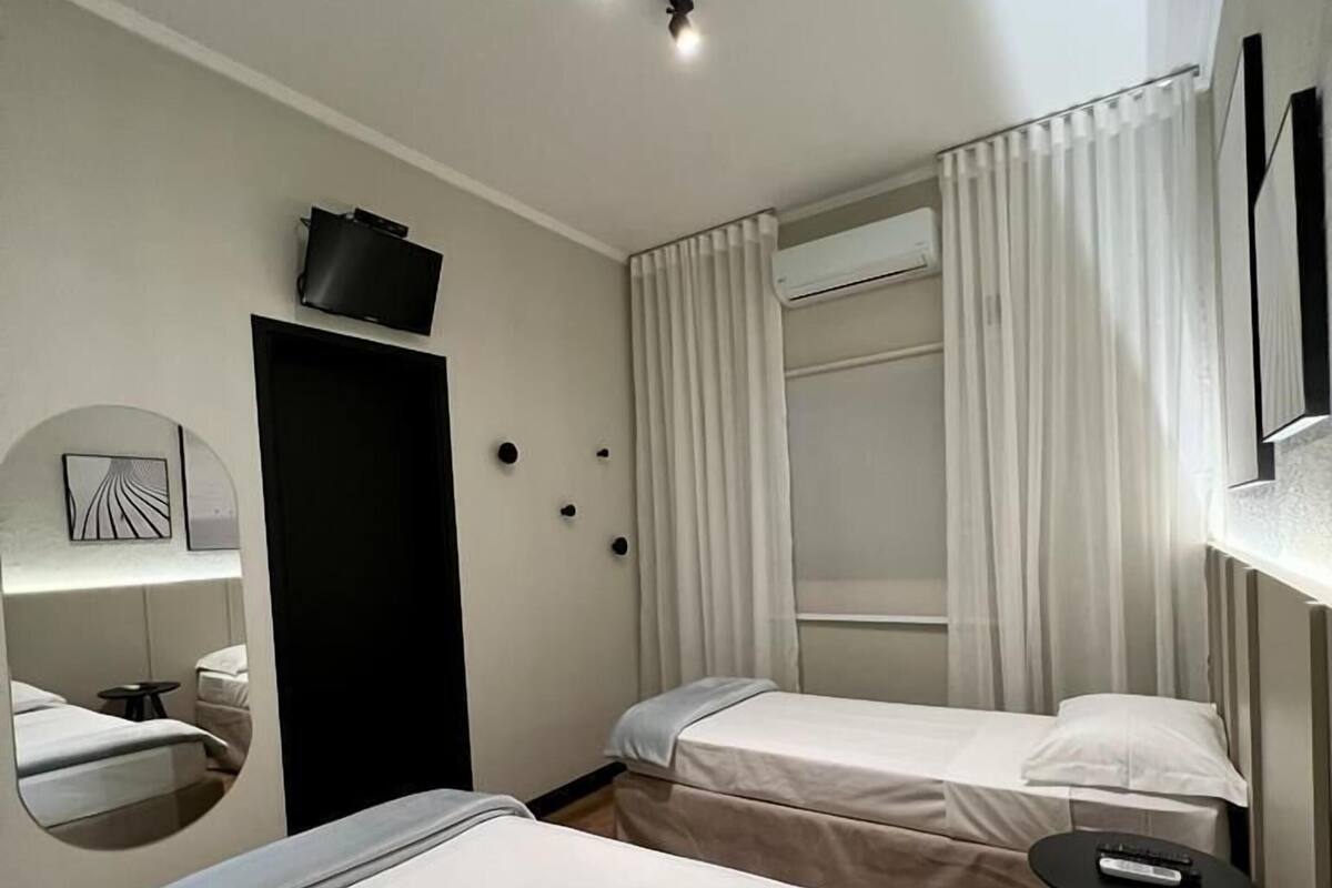 A hotel room with two beds, a mirror, a TV, an air conditioning unit, and a small table with a remote control.