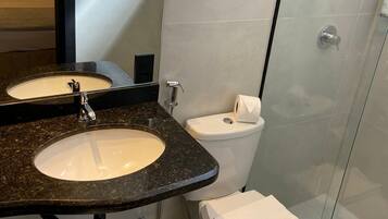 A modern bathroom with a granite countertop sink, a mirror, a toilet, and a glass shower enclosure.