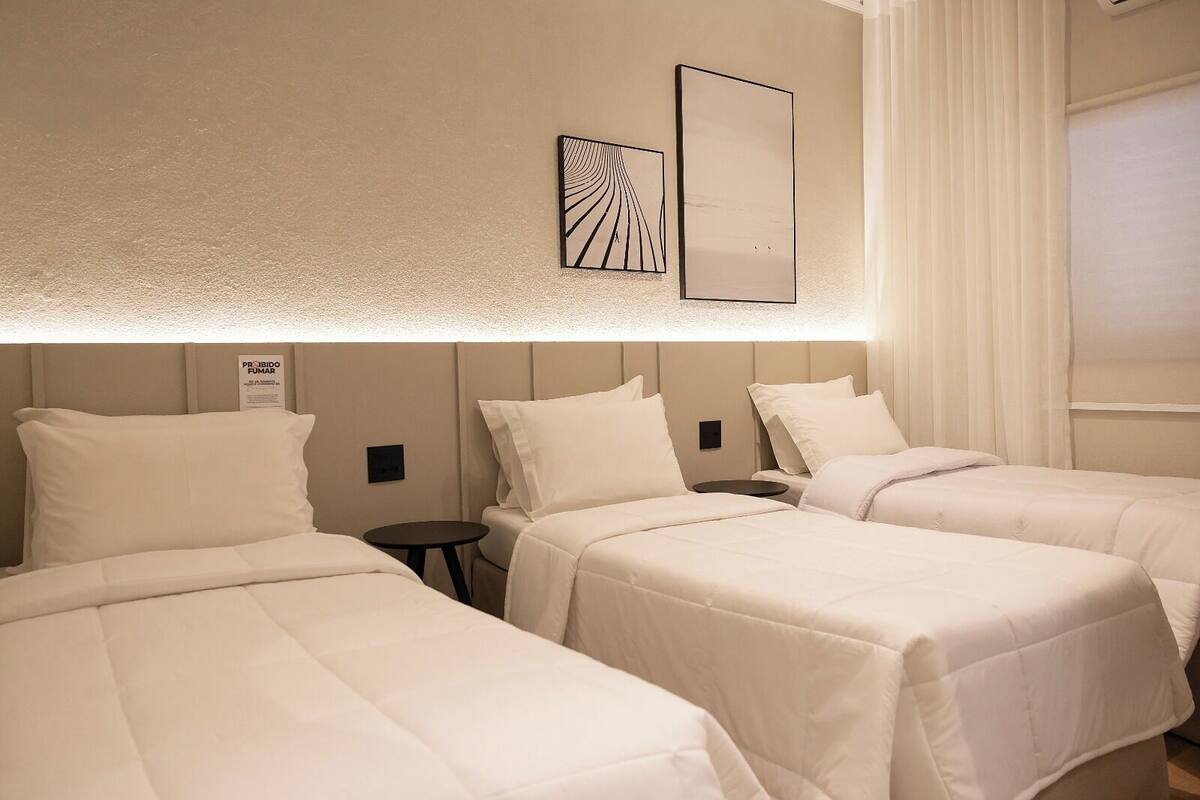 A hotel room with three beds, a small table, and a wall-mounted artwork.