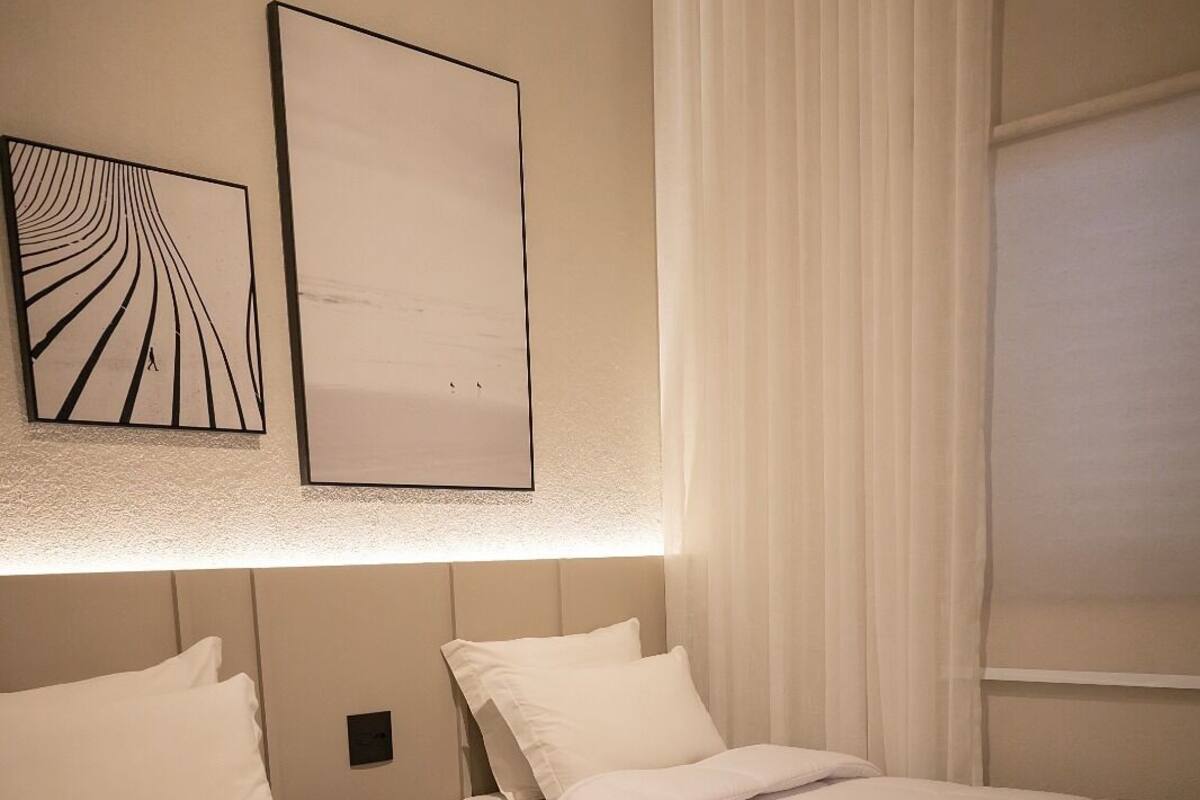 A hotel room with two beds, a bedside table, a wall-mounted artwork, and a window with curtains.