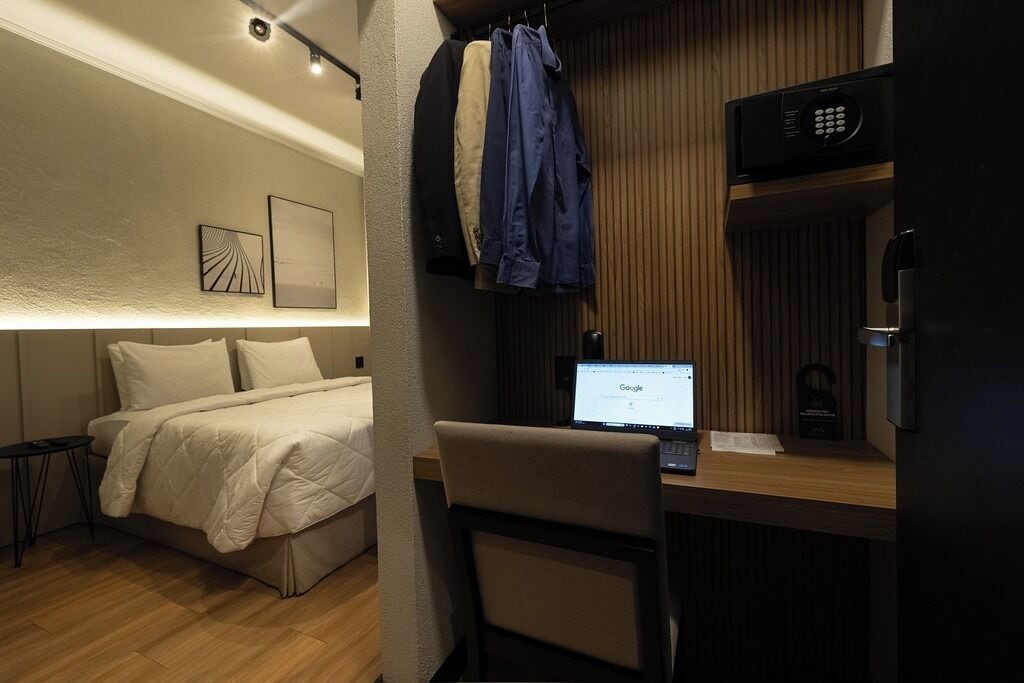 A bedroom with a bed, a desk with a laptop, and a microwave above the desk.