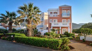 Un hotel de varios pisos con balcones, rodeado de jardines cuidados y palmeras.