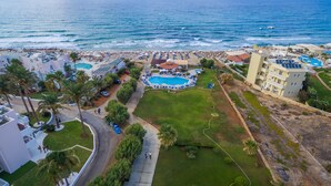 Vista aérea de un complejo turístico costero con piscina central, acceso a la playa y varios edificios.