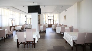 Un comedor amplio con varias mesas y sillas, ventanas grandes y un televisor de pantalla plana montado en la pared.