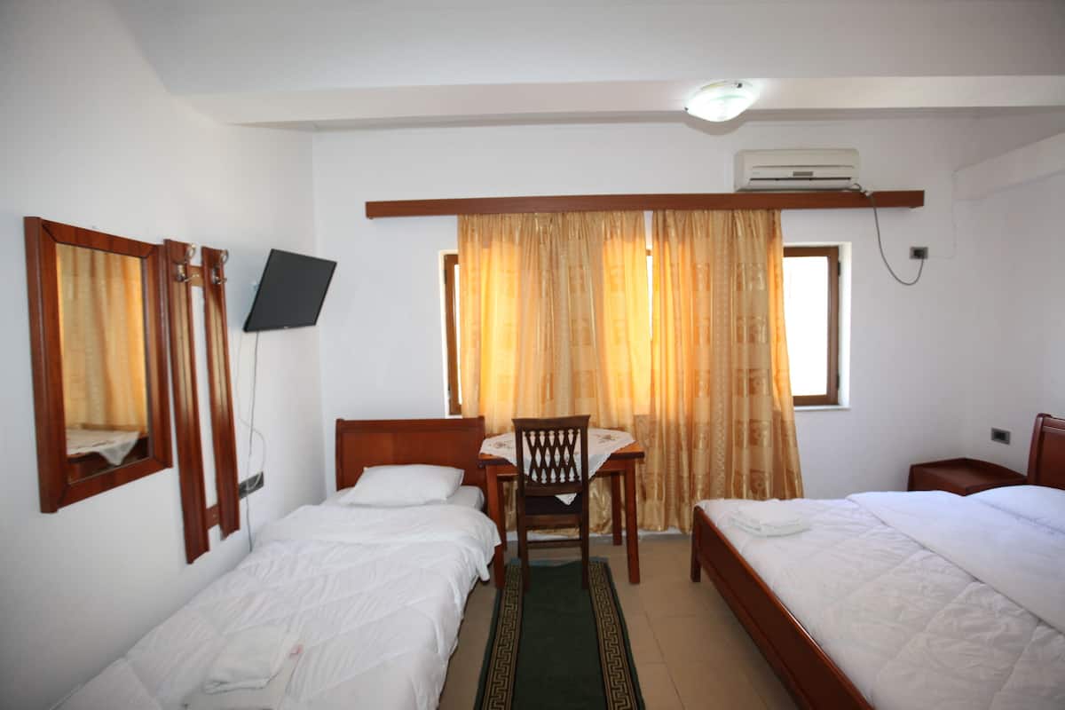 Quarto de hotel com duas camas, uma escrivaninha, uma cadeira, uma televisão e uma janela com cortinas.