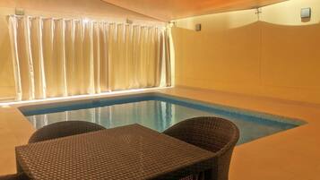 Una piscina interior con agua azul cristalina, rodeada de sillones de mimbre y una mesa.