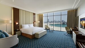 Habitación de hotel con una cama grande, un escritorio, una silla y vistas a un horizonte urbano y al agua.