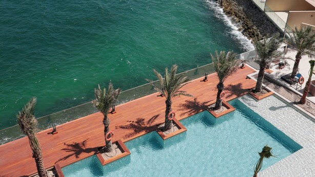 Un hotel frente al agua con piscina, palmeras y vista al horizonte de la ciudad.