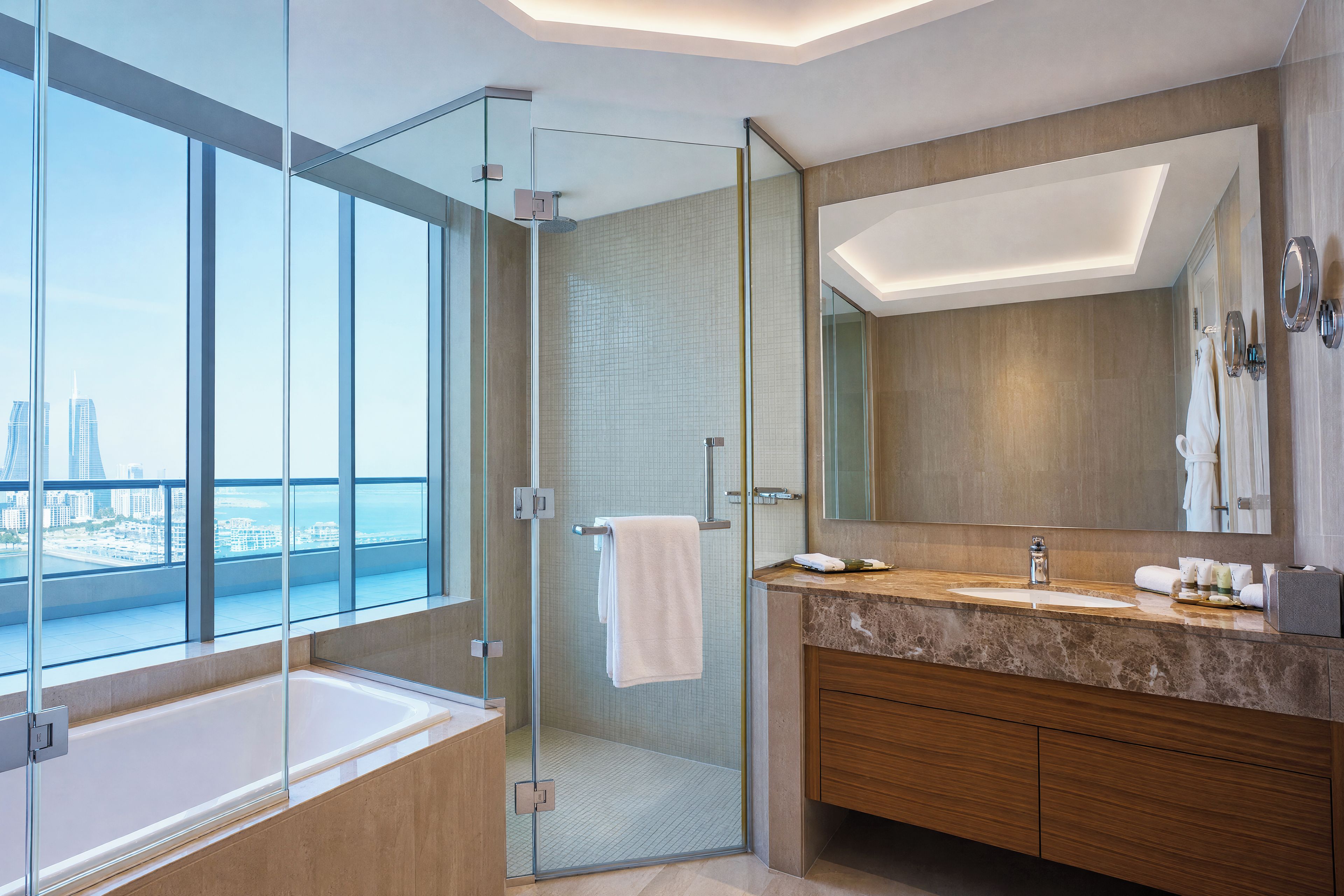 Un baño moderno con ducha envuelta en vidrio, un espejo grande y vistas a un paisaje urbano.
