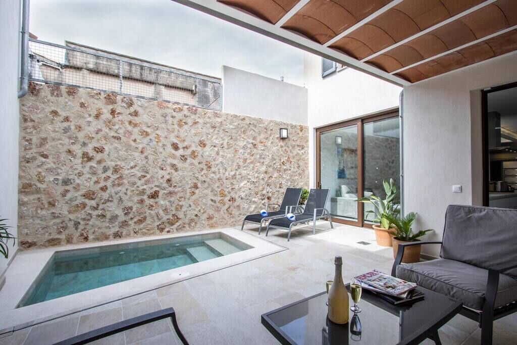 A modern outdoor living area with a stone wall, a small pool, lounge chairs, and a glass door leading to a patio.
