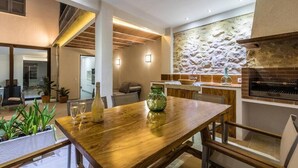 A modern kitchen with a stone wall backsplash, a built-in grill, and a wooden dining table with chairs. - Casa Bugera, Beautiful restored house in Pollensa (Pollença)
