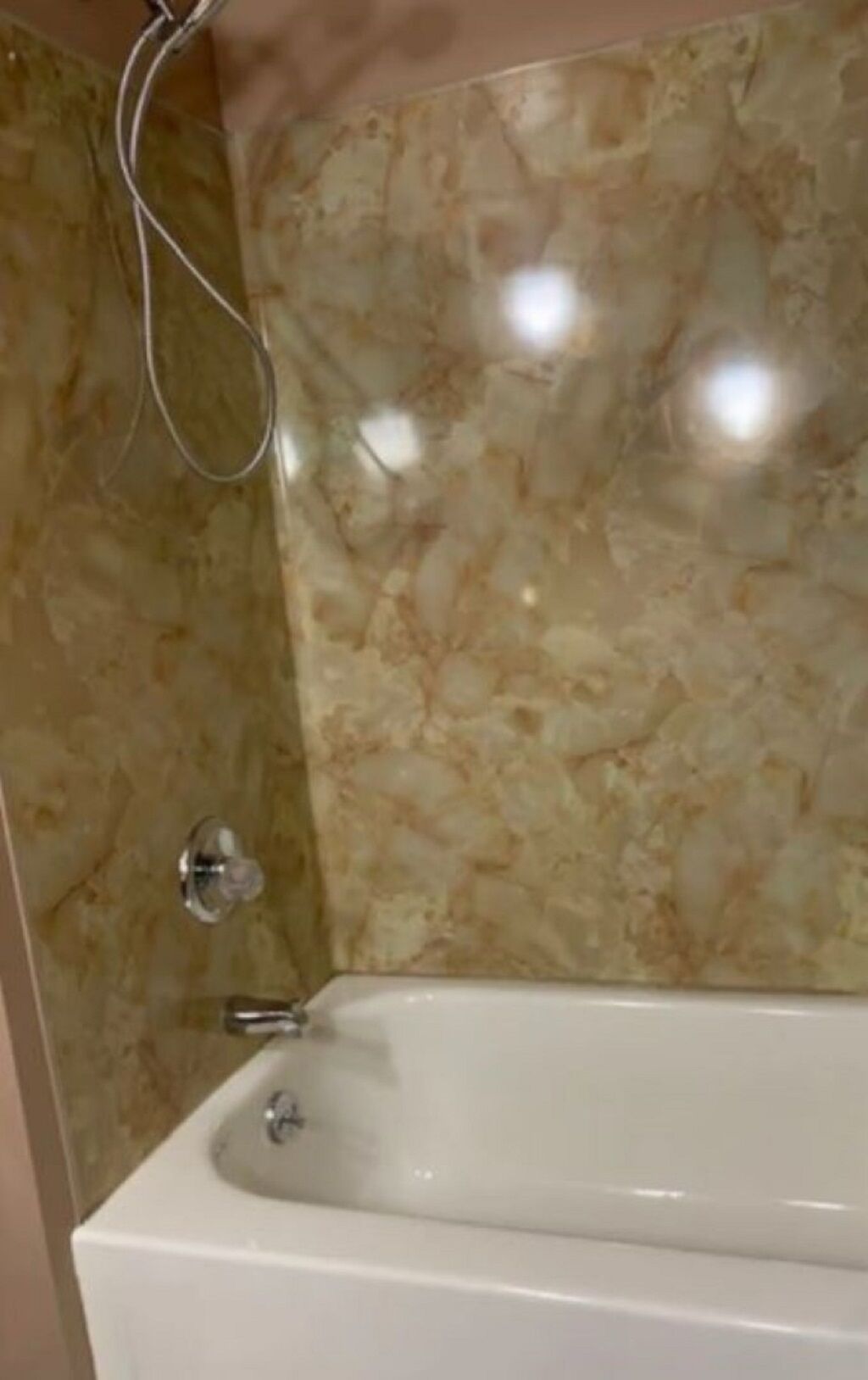 Un baño con pared de mármol y bañera blanca.