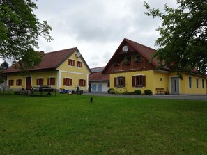 A yellow building with a red roof, a balcony with flowers, and a small lawn in front.