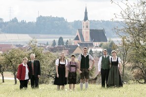 Een groep mensen staat in een grasveld, met een kerk en gebouwen op de achtergrond.