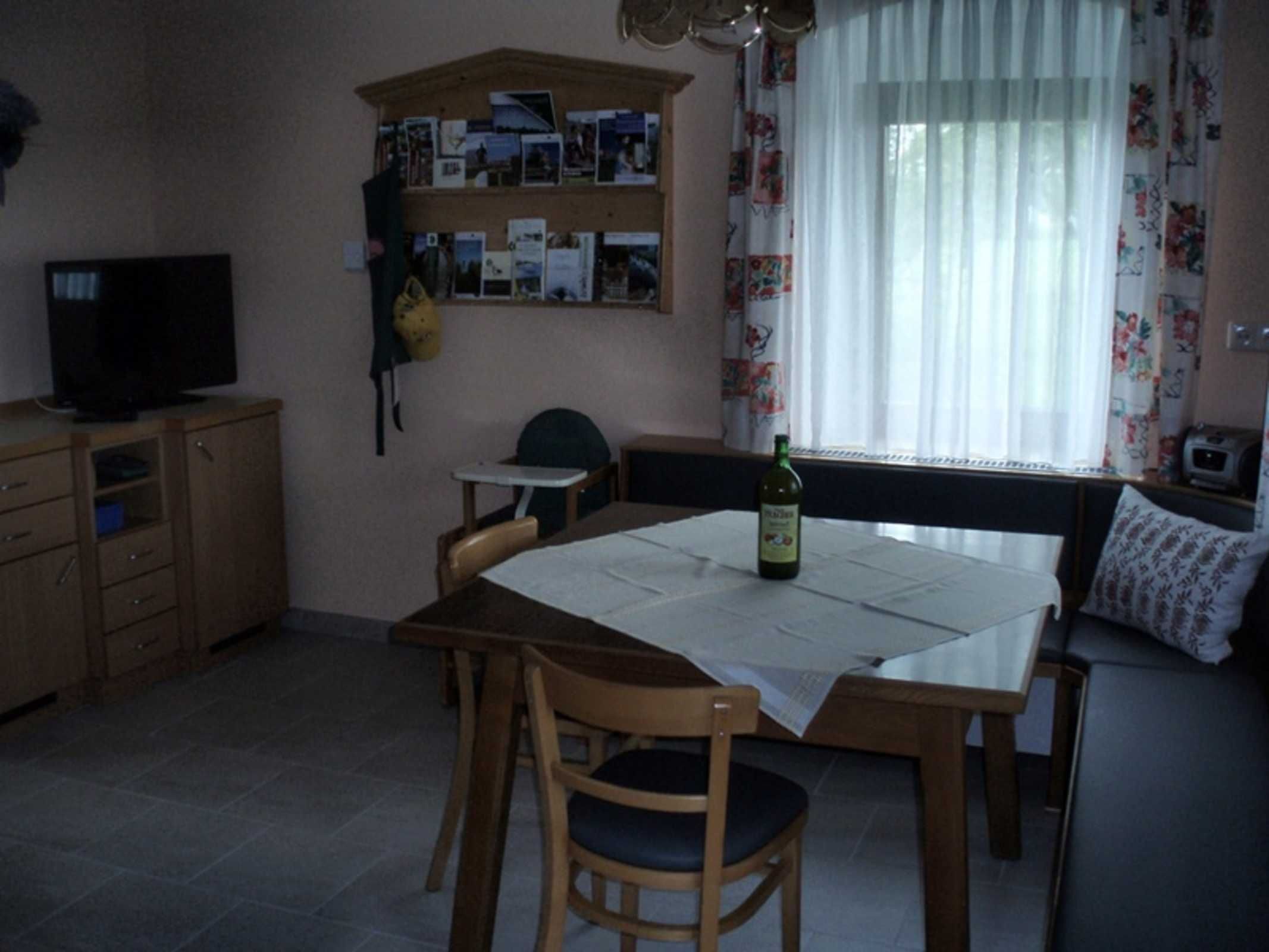 A small dining area with a table, chairs, a television, and a shelf with photos.