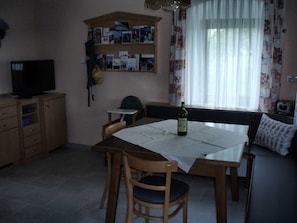 Een gezellig eethoekje met een tafel, stoelen, een televisie en een plank met foto's.