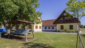 A two-story building with a balcony, a swing set, and a well-maintained lawn. - Vacation apartment - Ermi/Pracher (Petzelsdorf in der Weststeiermark)