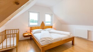 A bedroom with a wooden bed, two windows, a crib, and a radiator. - Vacation apartment - Ermi/Pracher (Petzelsdorf in der Weststeiermark)