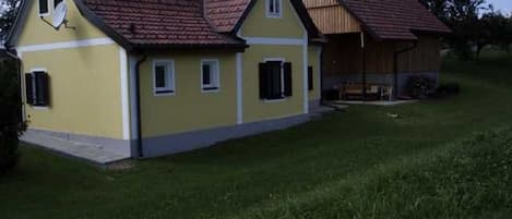 A yellow building with a red roof, a covered porch, and a grassy yard.
