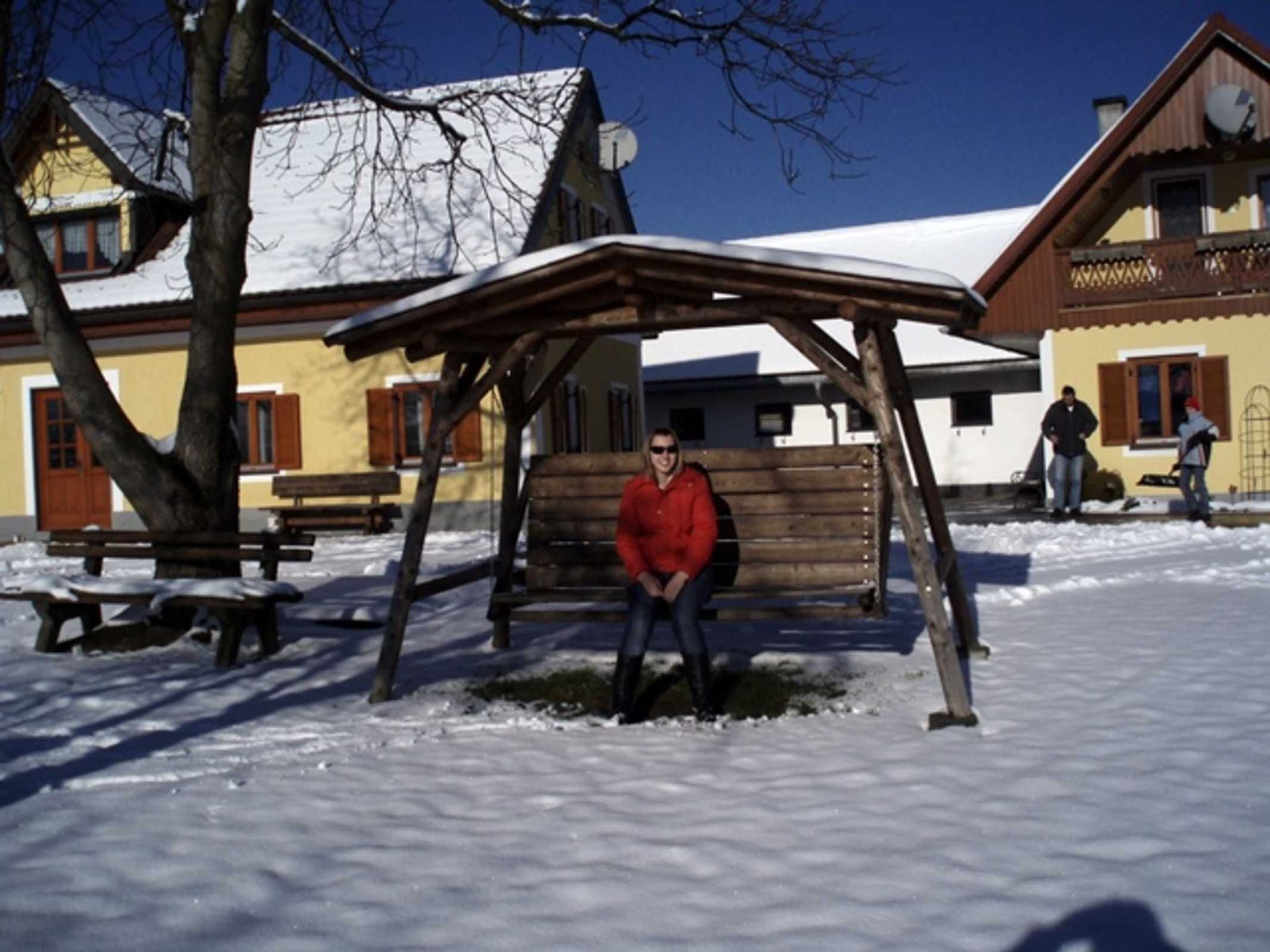A wooden bench under a shelter in a snowy outdoor area with buildings in the background.
