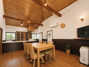 Una habitación amplia con techo de madera, una mesa de comedor con sillas, un televisor y un reloj en la pared.