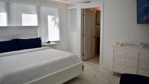 A bedroom with a large bed, a nightstand, a dresser, and a door leading to a closet. - Sweet Caroline Historic Seaport Key West Home Rental Floor 1 (Key West)