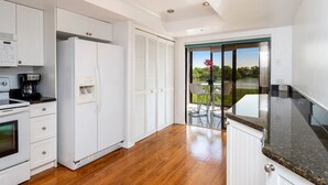 A modern kitchen with white cabinetry, a built-in oven, a coffee maker, and a view of a lake through a sliding glass door. - Blue Lagoon Estate (Fort Myers Beach)