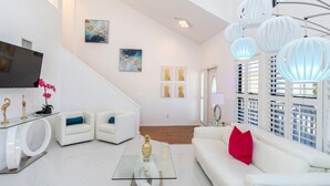A modern living room with a staircase, white furniture, and artwork on the walls. - Blue Lagoon Estate (Fort Myers Beach)