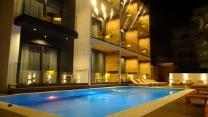 Ein modernes Hotel mit Poolbereich, mehreren Liegestühlen und einer Glasbrüstung.