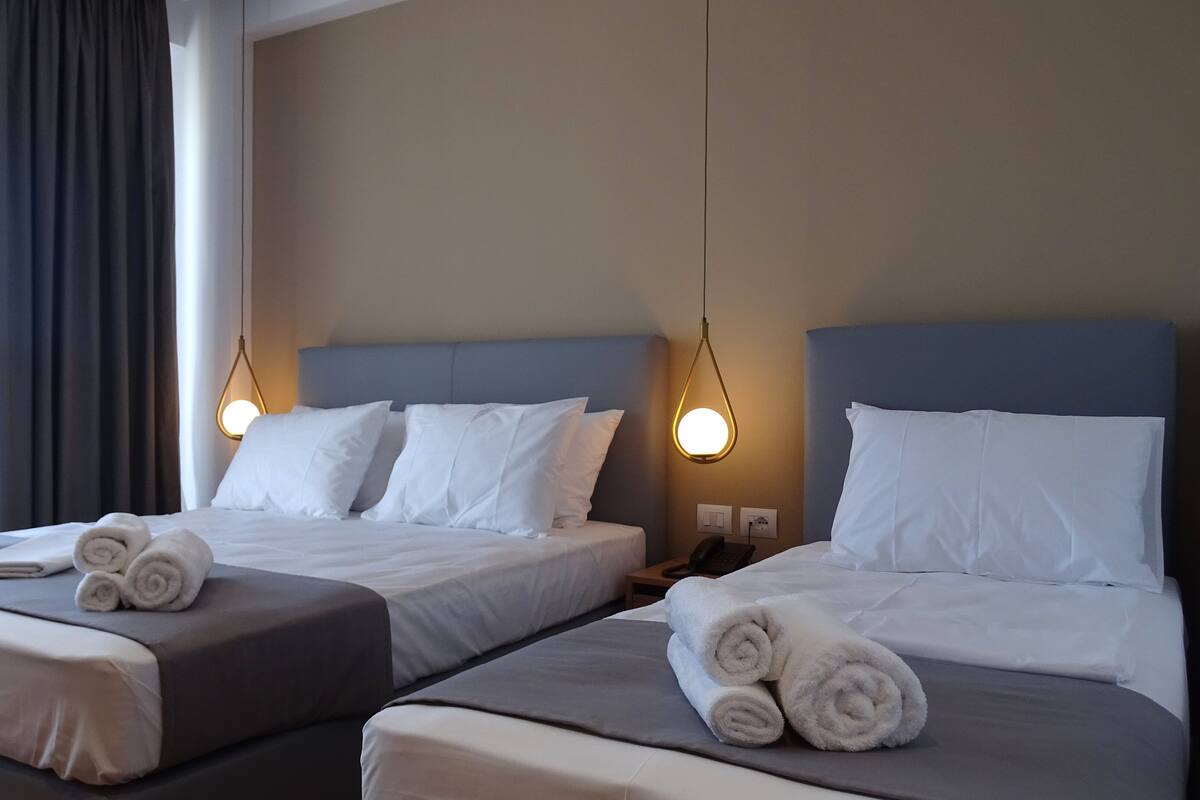 Two twin beds with white linens, a bedside table with a lamp, and a window with curtains.