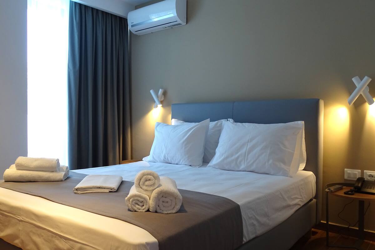A hotel room with a bed, towels, a bedside table with a phone, and an air conditioning unit.
