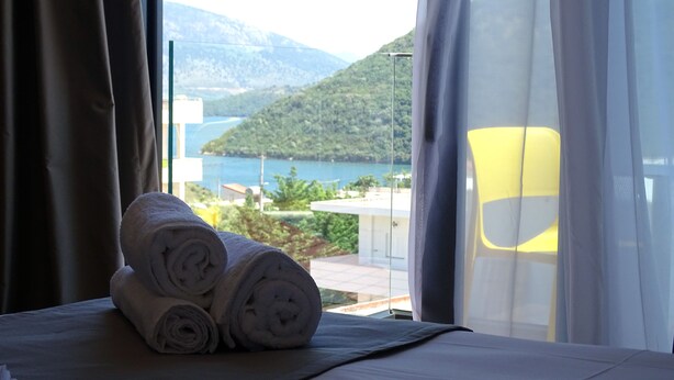 Ein Bett mit aufgerollten Handtüchern und Blick auf einen See und Berge durch ein Fenster.