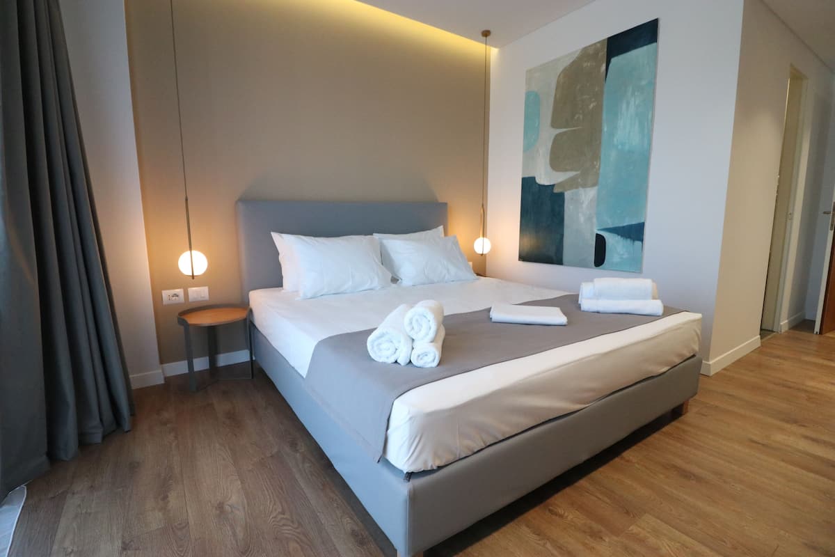 A modern hotel room with a large bed, bedside tables, a wall art piece, and a wooden floor.