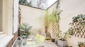 Une table en verre avec des chaises, une petite plante en pot et une clôture en bambou dans une cour.