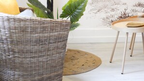 Un salon comprenant une console noire, un fauteuil en osier, une table ronde en bois et un mur orné d’une fresque à motifs.