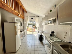 A compact kitchen with a refrigerator, microwave, stove, and sink. There is a dining area with a table and chairs, and a view of the outdoors through a glass door.