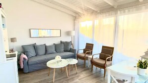 Ein Wohnzimmer mit grauem Sofa, zwei Sesseln, einem kleinen runden Tisch und einem weißen Tisch.